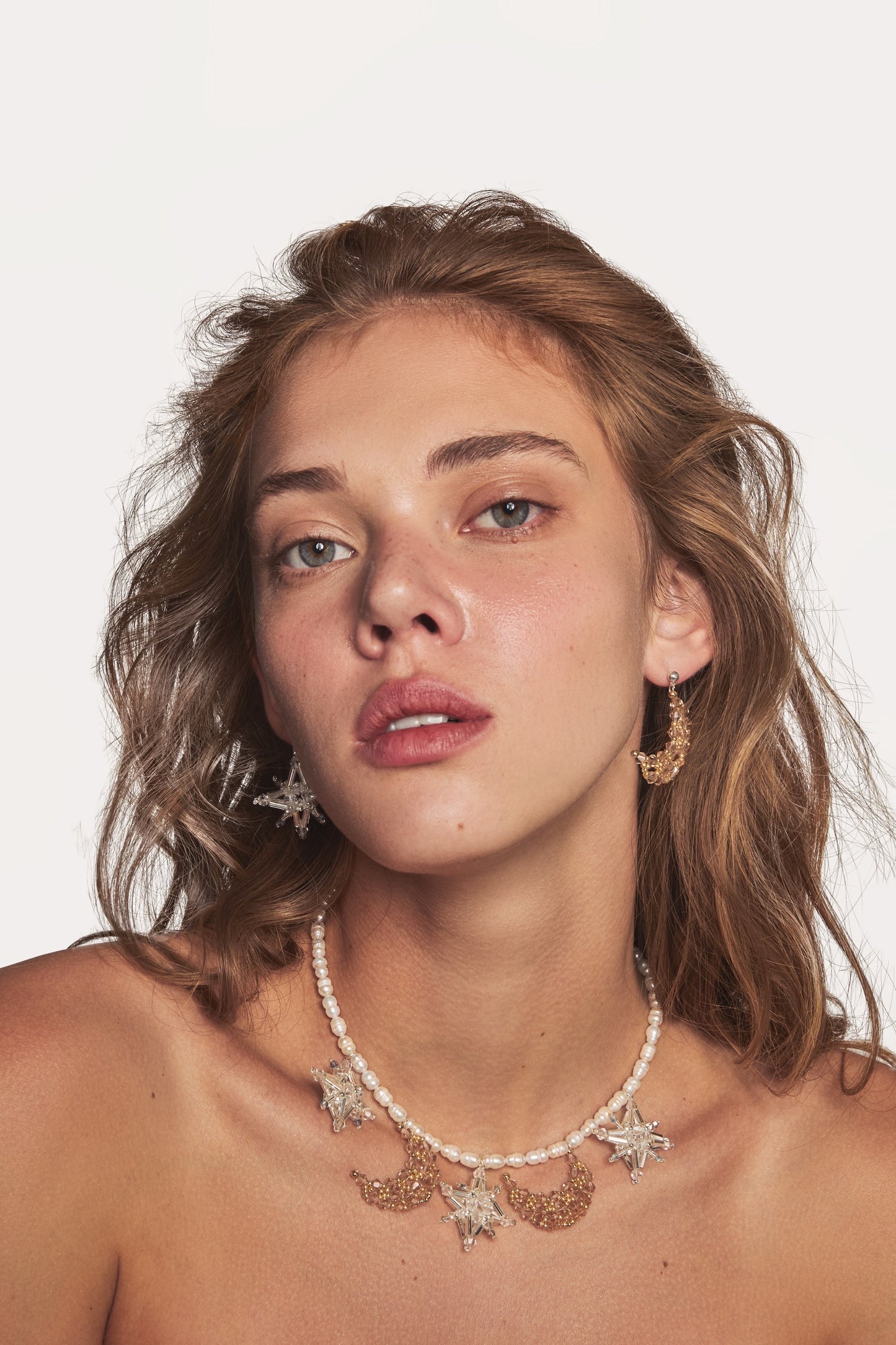 Pearl necklace worn with star and crystal charms; delicate sparkle around the neckline.