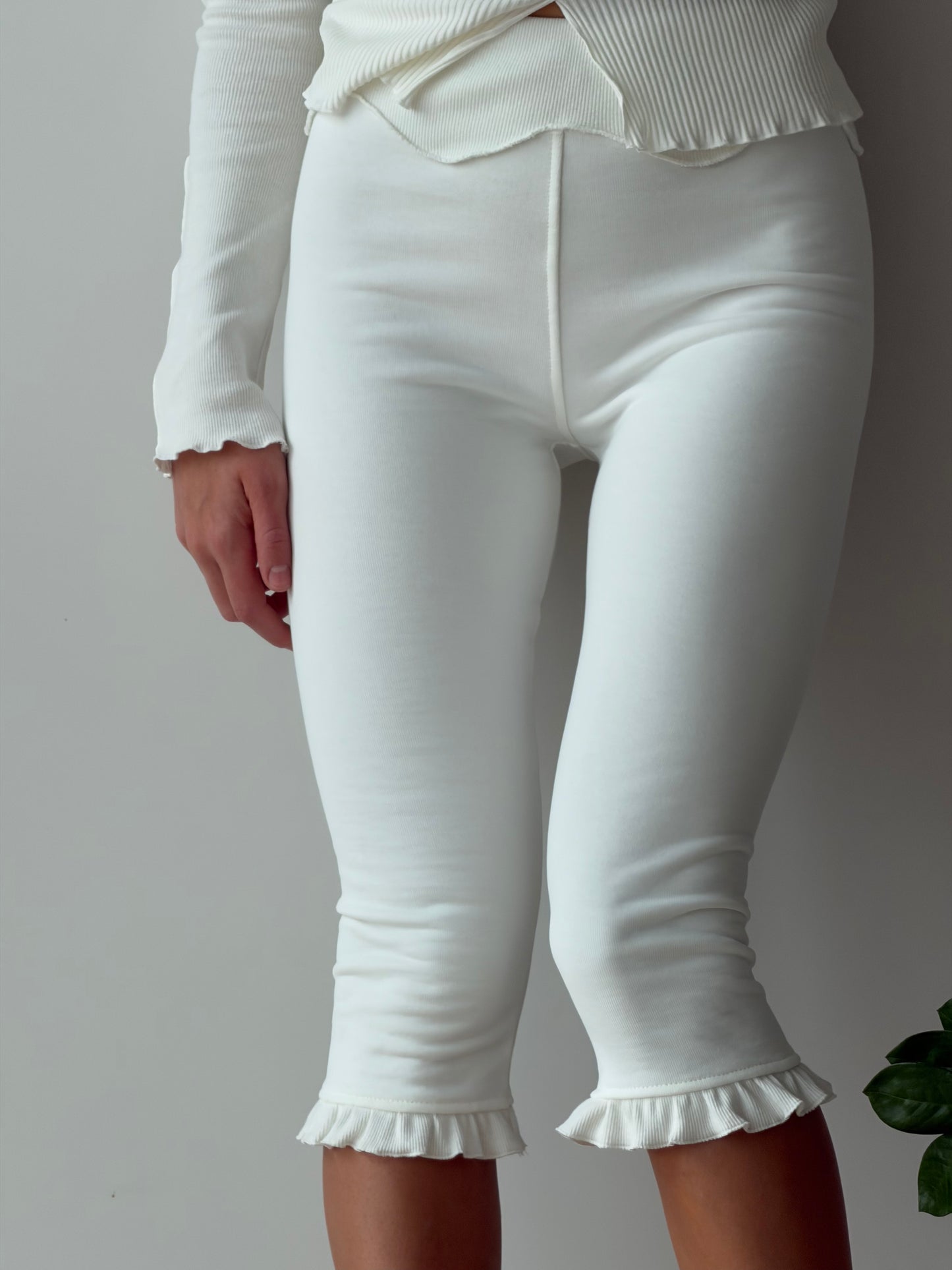 White capri pants close-up: vertical seam and ruffled scalloped cuff hem.