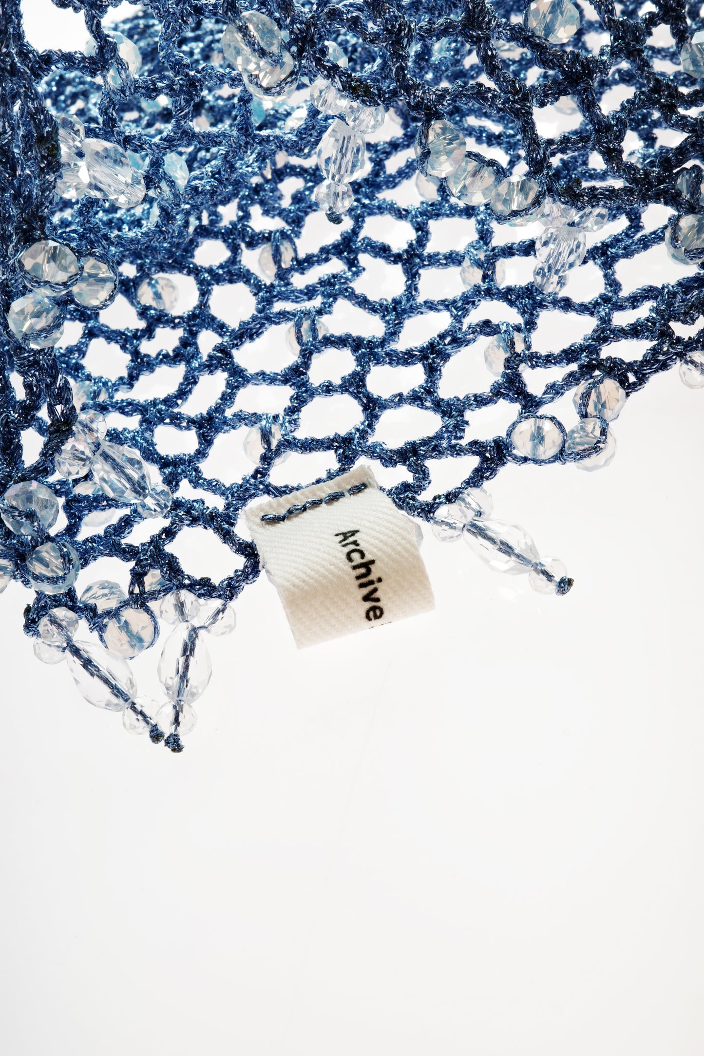 Blue boho crochet hat close-up with openwork pattern, fabric tag and dangling fringe.