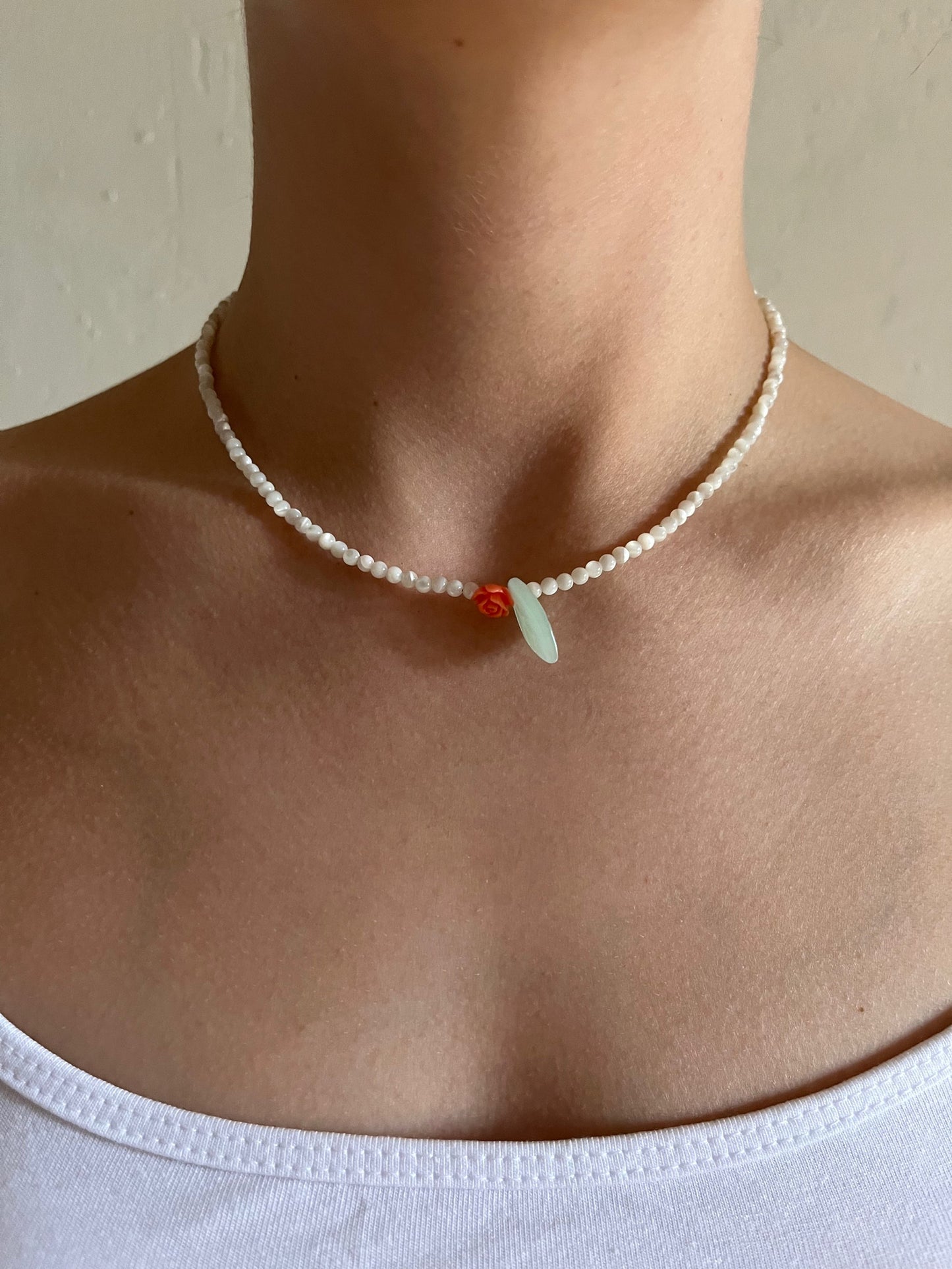 Close-up of pearl bead necklace with red rose pendant and green leaf at the throat