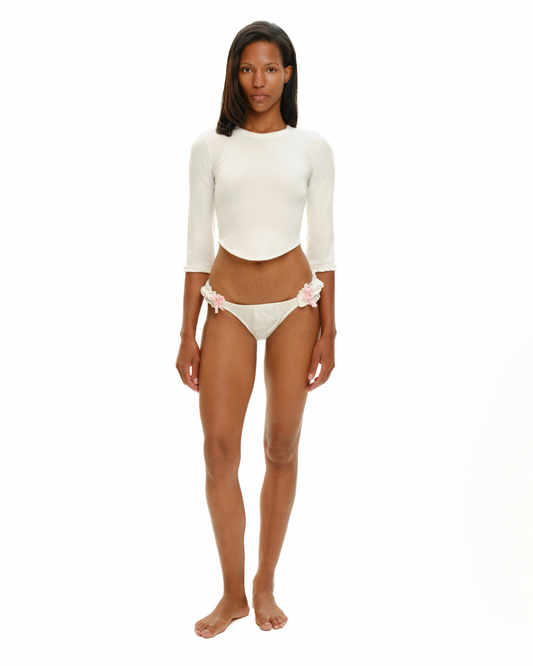 White long-sleeve crop top with scalloped cuffs, paired with bikini briefs and pink bow accents