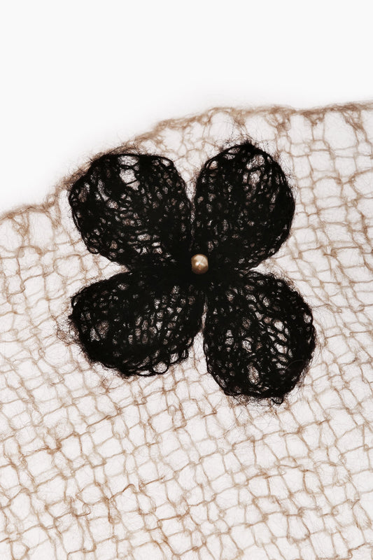 Beige scarf fabric close-up with black clover flower and small pearl center